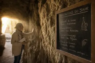 Handwritten chalk board on a limestone cellar wall with a visitor gently touching the stone in soft, natural cave light