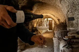 Vigneron’s hands pouring crémant in a rustic troglodyte cellar at dusk, soft golden light illuminating rising bubbles and stone textures.